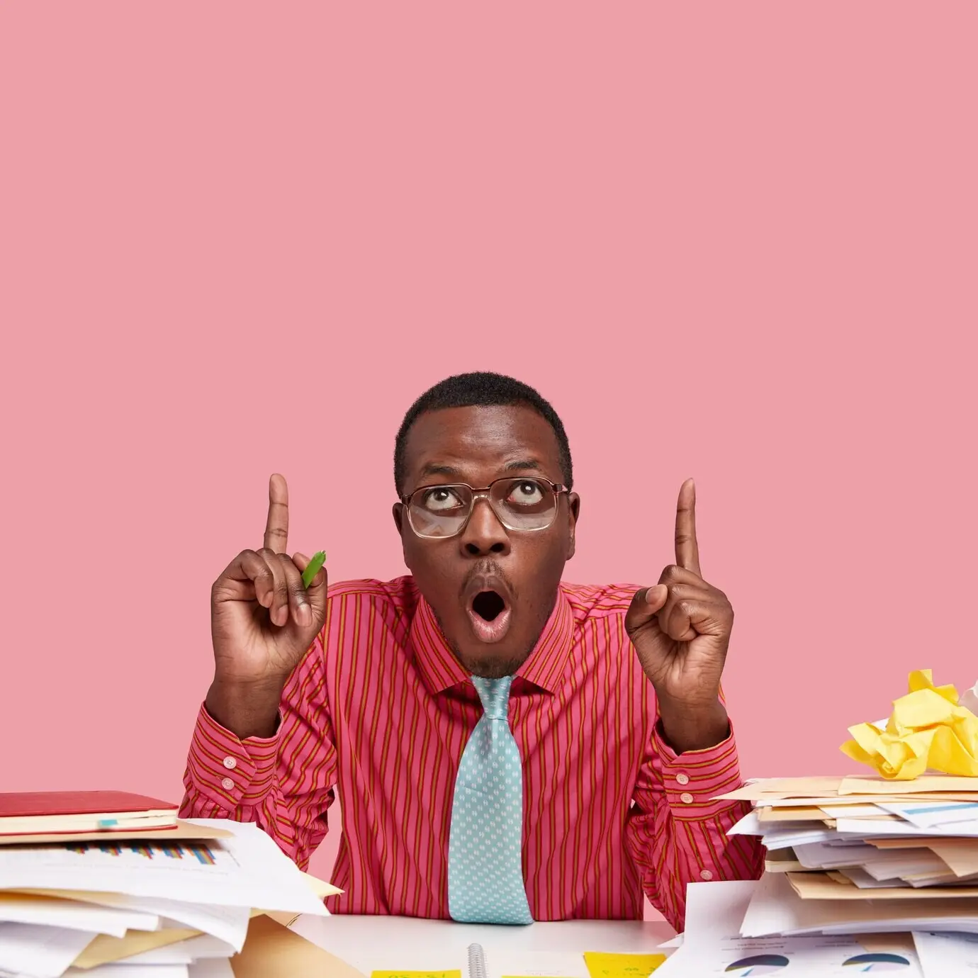 Portrait-oriented photo of a dumbfounded black man, mouth agape in amazement, pointing both index fingers upward as he notices something unexpected on the ceiling.
