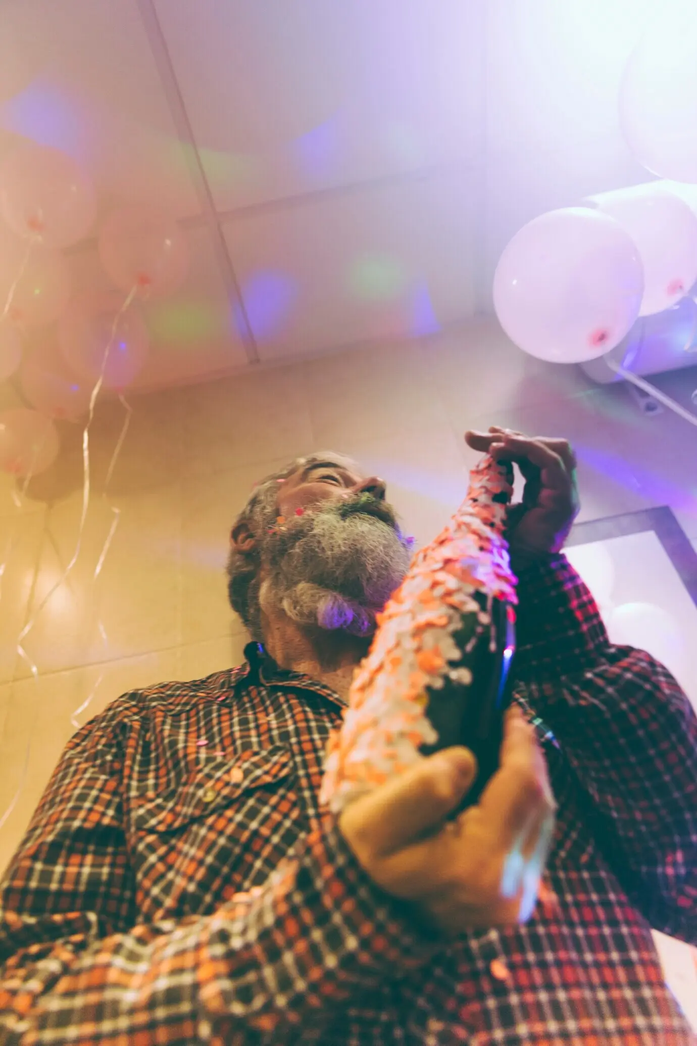 Low-angle view of a senior man holding a bottle of alcohol, his hand decorated with confetti.